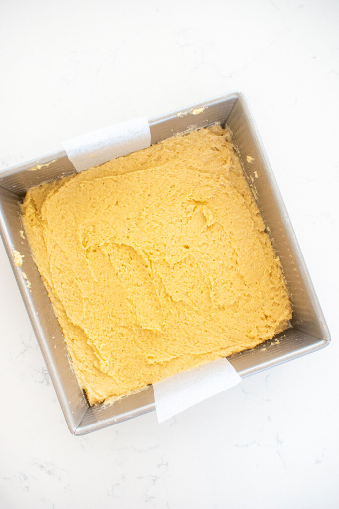 sugar cookie dough pressed into a square baking pan on a white marble counter.