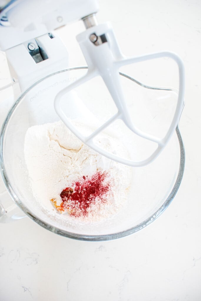 ingredients for pink frosting in a glass mixing bowl on a white marble counter.
