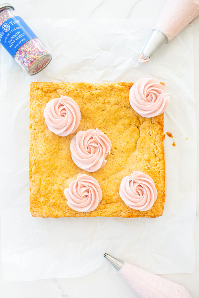 organic sugar cookie bars with frosting being decorated with pink frosting roses on white parchment paper.