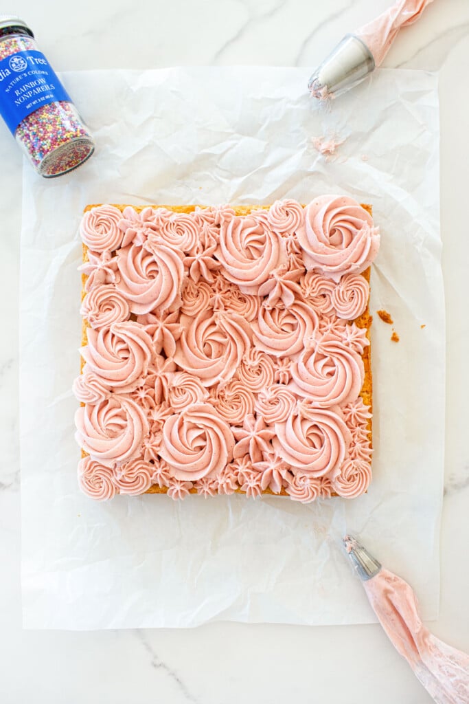 organic sugar cookie bars with frosting being decorated with pink frosting roses on white parchment paper.