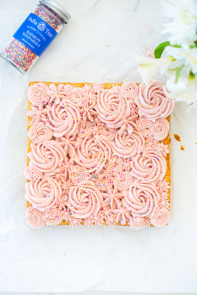 organic sugar cookie bars with frosting being decorated with pink frosting roses on white parchment paper.