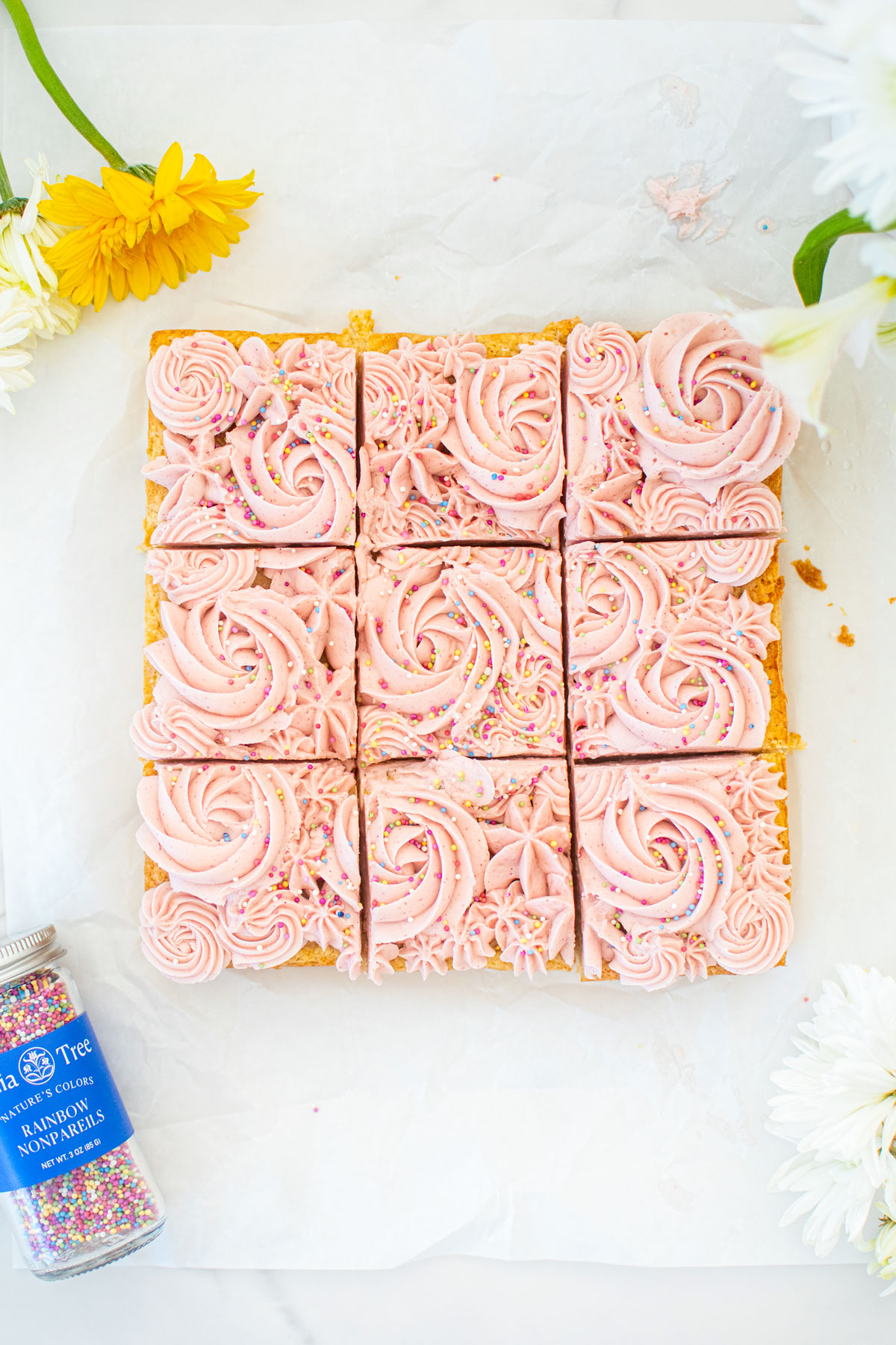 organic sugar cookie bars with frosting cut into 9 squares on a white parchment paper.