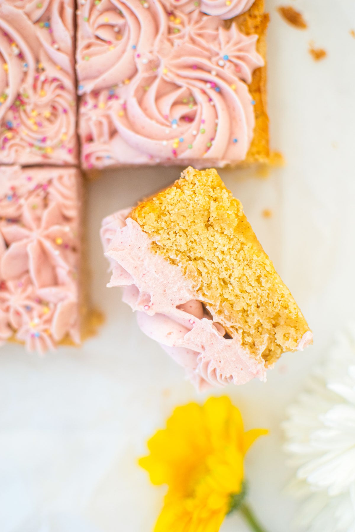 organic sugar cookie bars with frosting on a white parchment paper with fresh flowers.