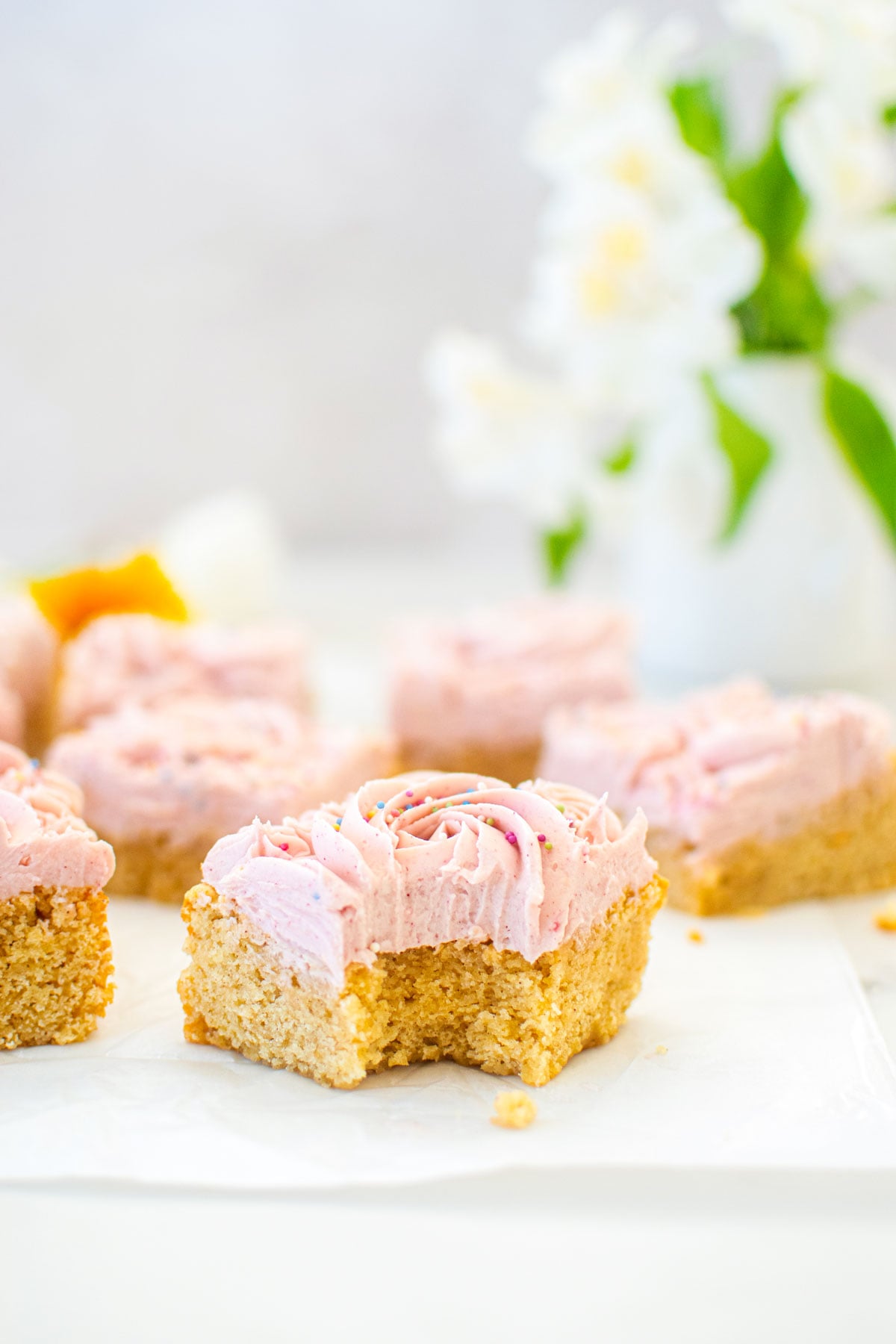 organic sugar cookie bars with frosting on a white marble counter one slice with a bite taken out.