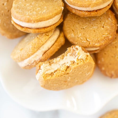 peanut butter oatmeal sandwich cookies on a white ruffle plate on marble counter.