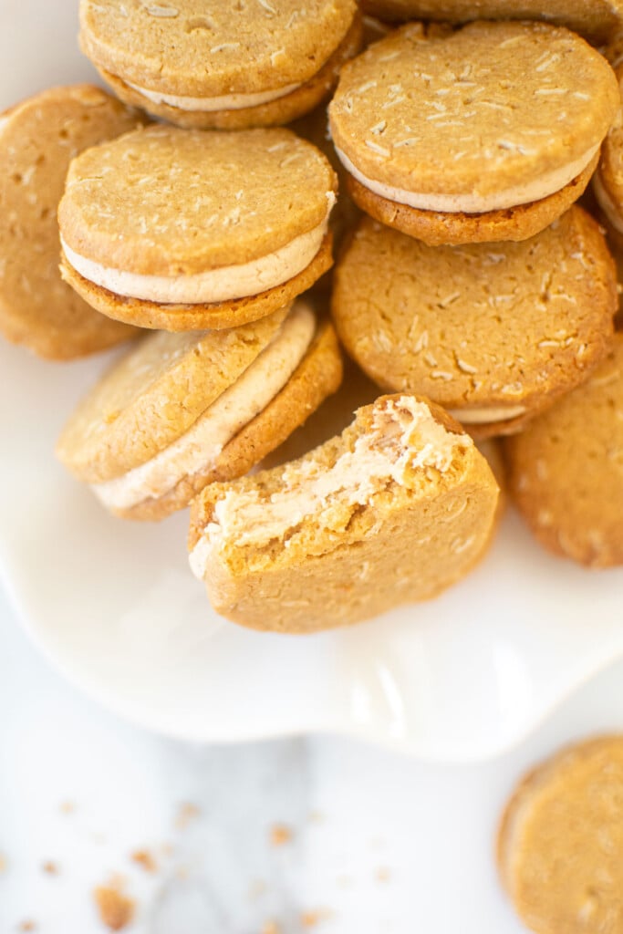 peanut butter oatmeal sandwich cookies on a white ruffle plate on marble counter.