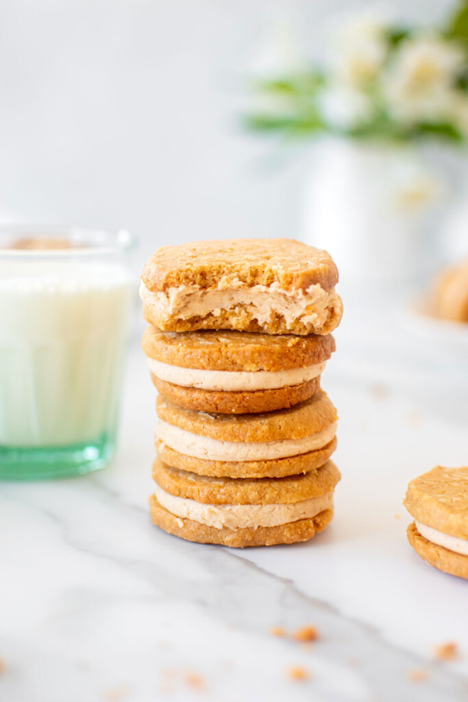 peanut butter oatmeal sandwich cookies stacked on a white marble counter with a glass of milk.