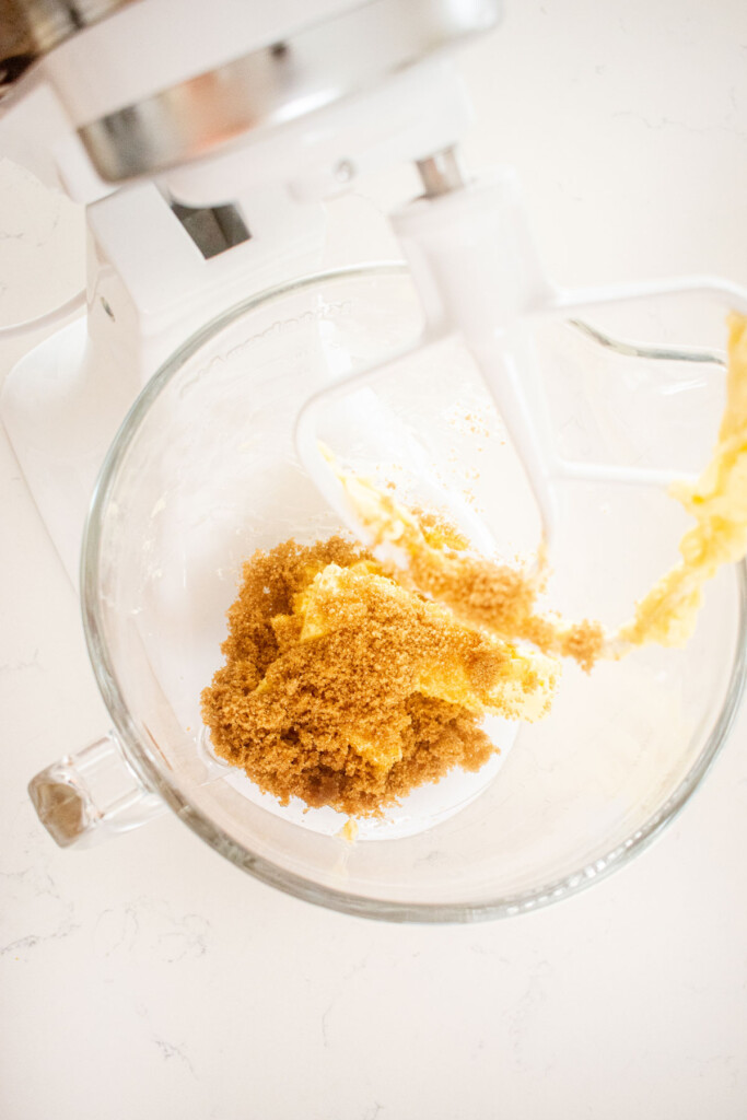 butter and brown sugar in a stand mixing bowl on a white marble counter.