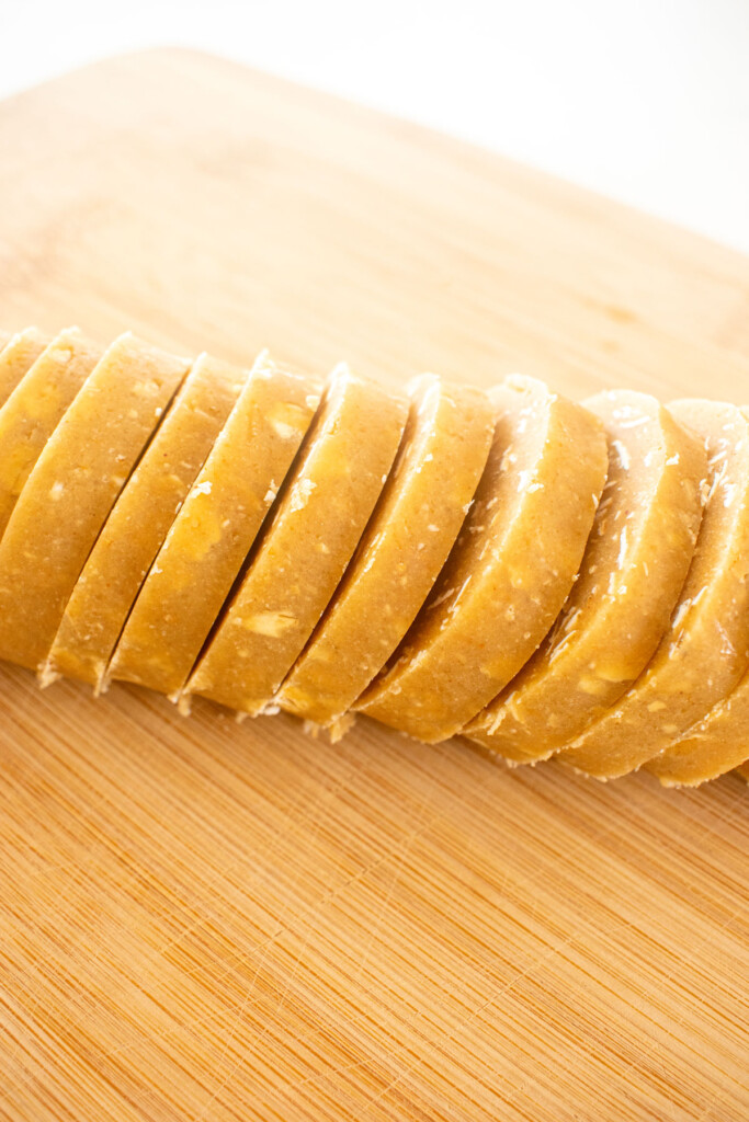 peanut butter oatmeal cookie dough sliced into slices on a wood cutting board.