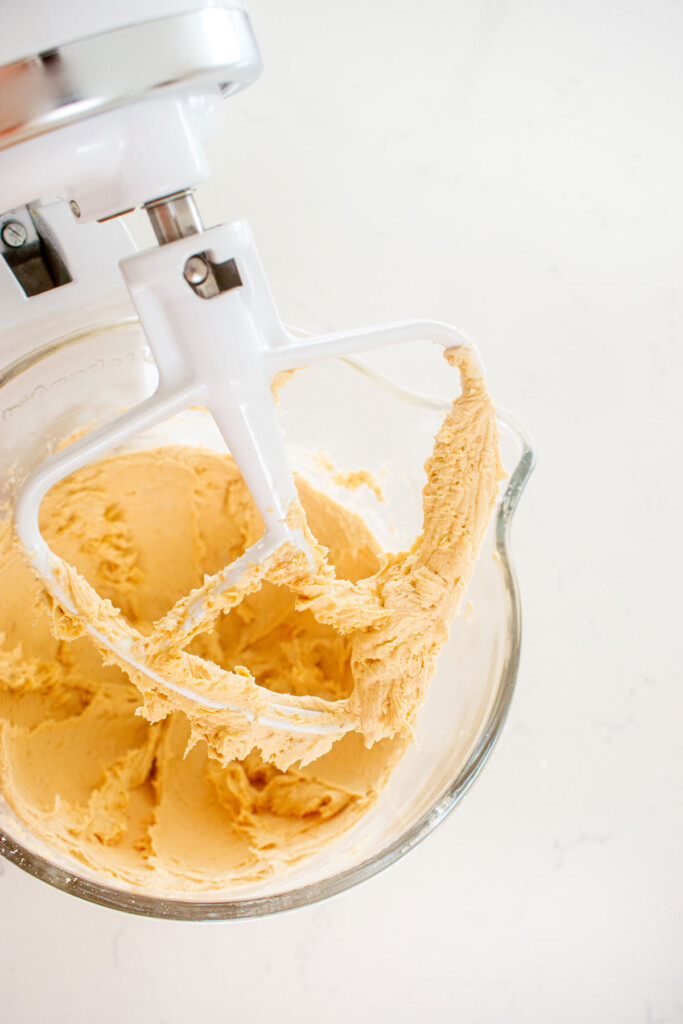 peanut butter frosting in a glass mixing bowl on a white marble counter.