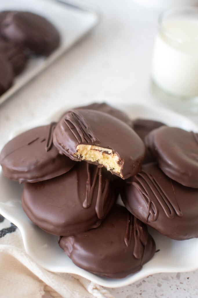 homemade tagalong cookies on a plate one with a bite taken out and a glass of milk on a marble counter.