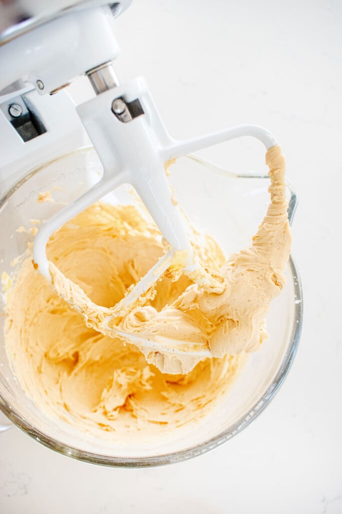 peanut butter frosting in a glass mixing bowl on a white marble counter.