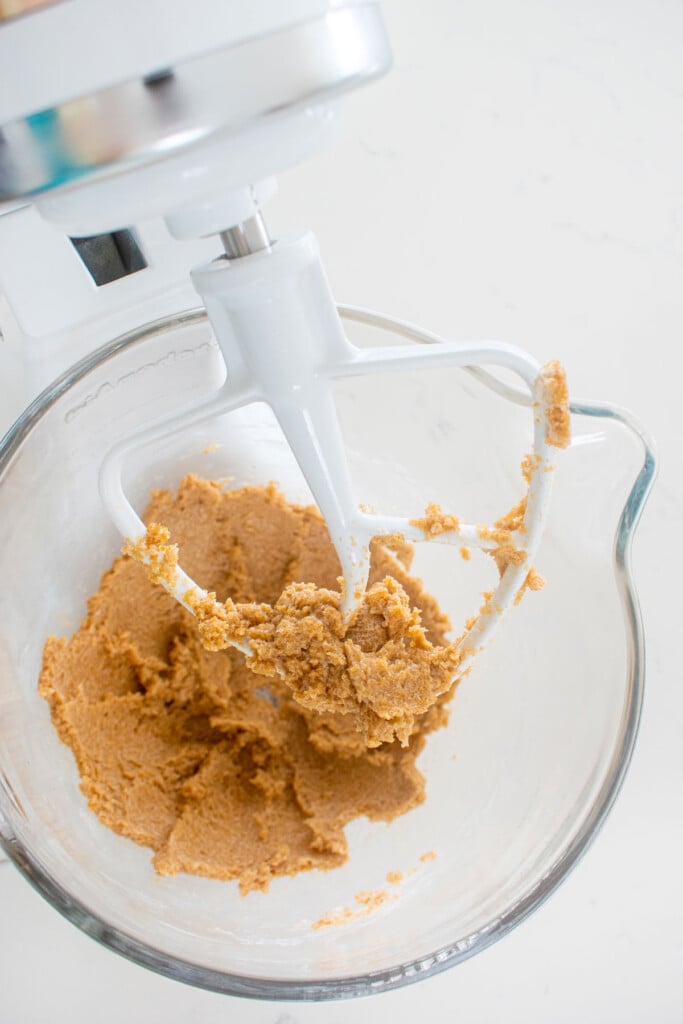 creamed vegan butter and sugar in a glass mixing bowl on a white marble counter.