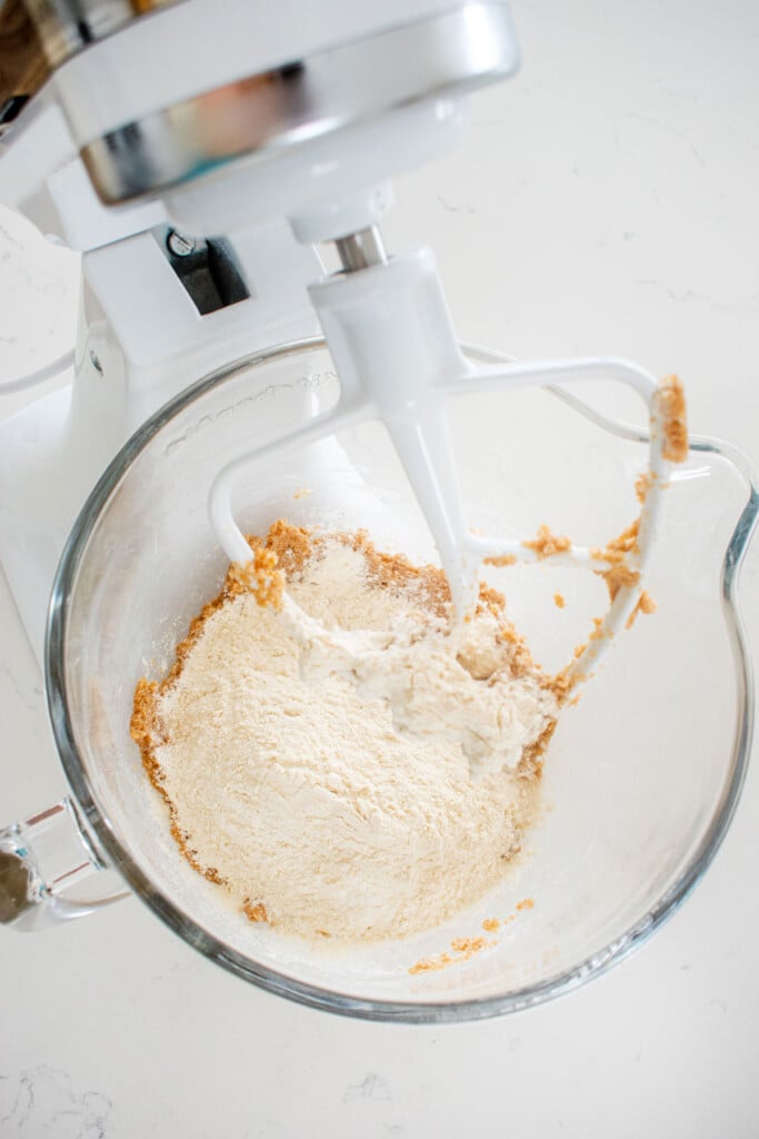 ingredients for vegan sourdough chocolate chip cookie dough in a stand mixing bowl on a white marble counter.