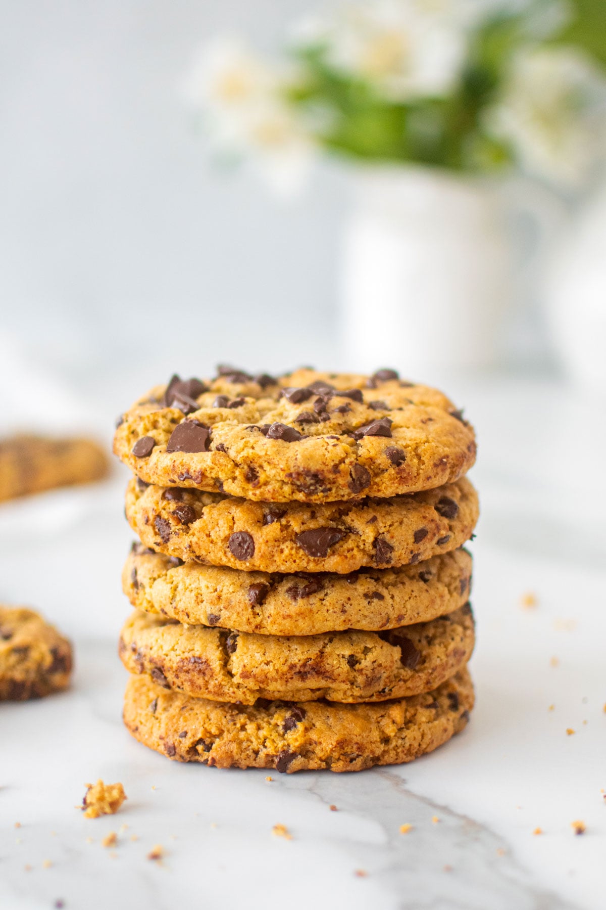 stack of vegan sourdough chocolate chip cookies on a white marble counter with fresh flowers.