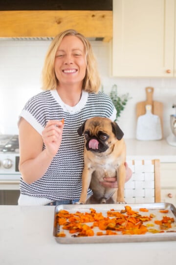 woman feeding pug veggie dog treats at the kitchen counter.