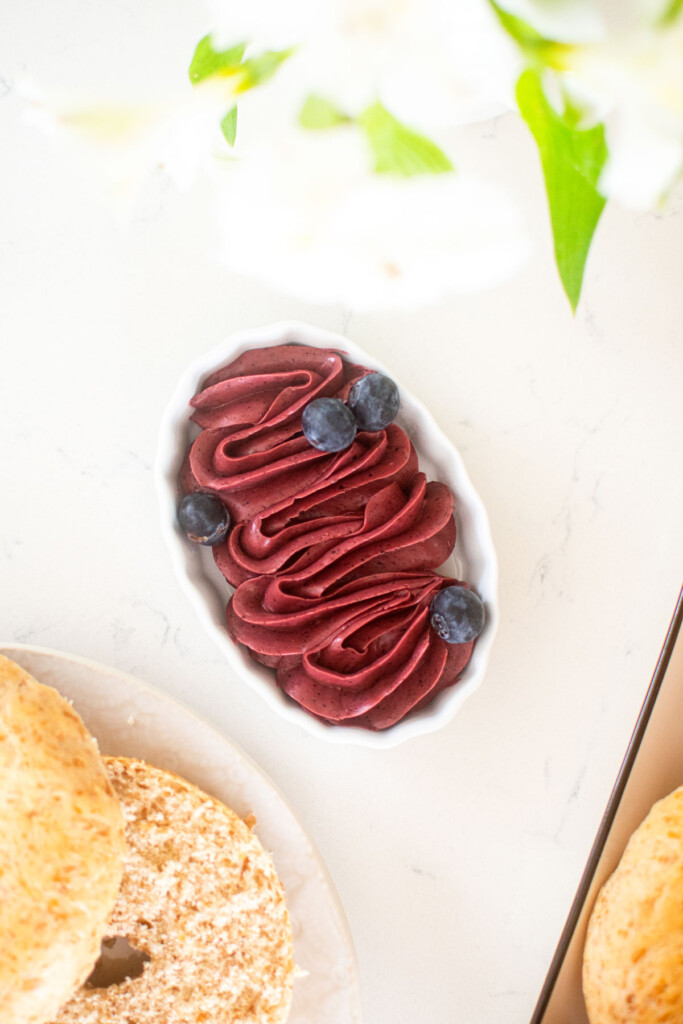 blueberry butter spread piped into a small white dish on a marble counter with bagels on the side.