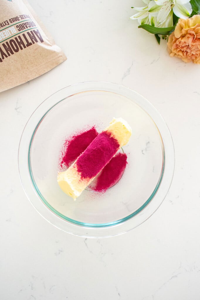 glass bowl with butter and blueberry powder on a marble counter.