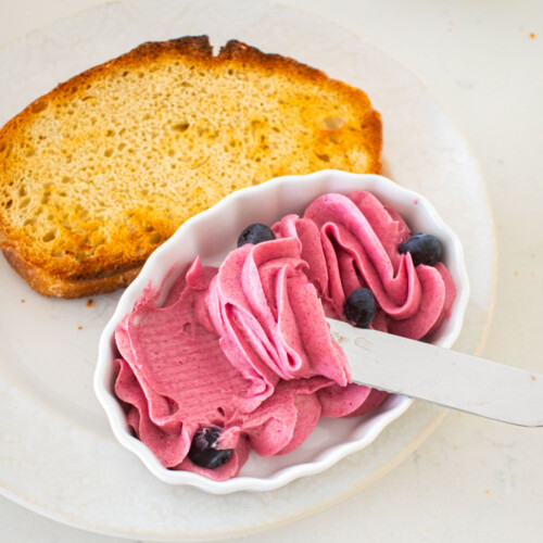 plate with toasted sourdough bread and a small dish with blueberry butter spread and a butter knife on a marble counter.