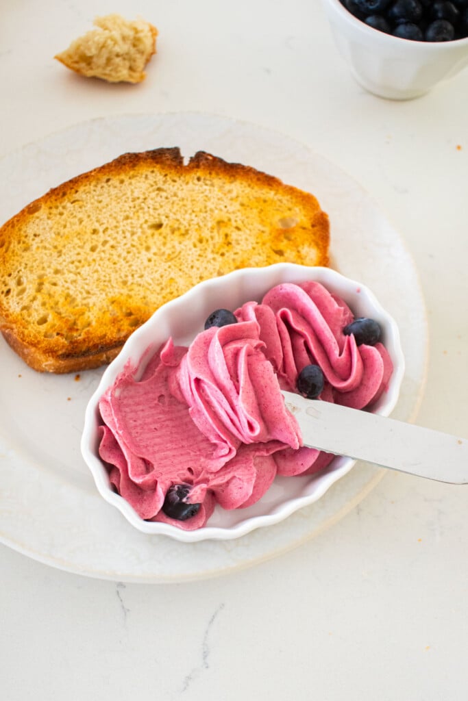 plate with toasted sourdough bread and a small dish with blueberry butter spread and a butter knife on a marble counter.