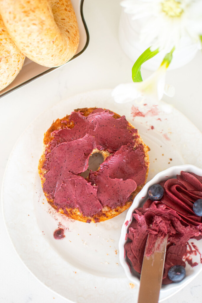 blueberry butter spread onto a toasted bagel on a white plate.