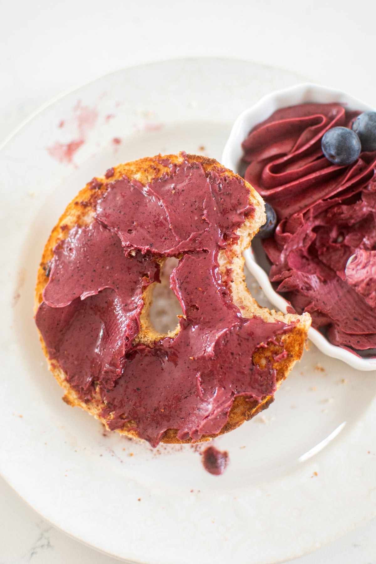 blueberry butter spread on a bagel with a bite taken out on a white plate.