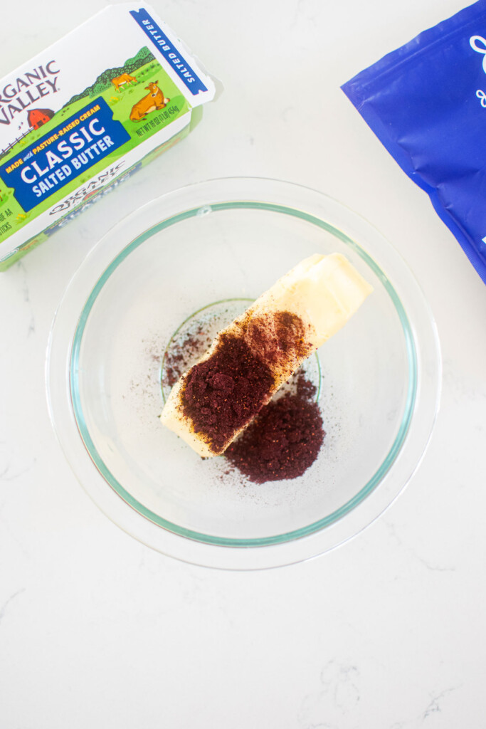 butter and wild blueberry powder in a glass mixing bowl on a white marble counter.