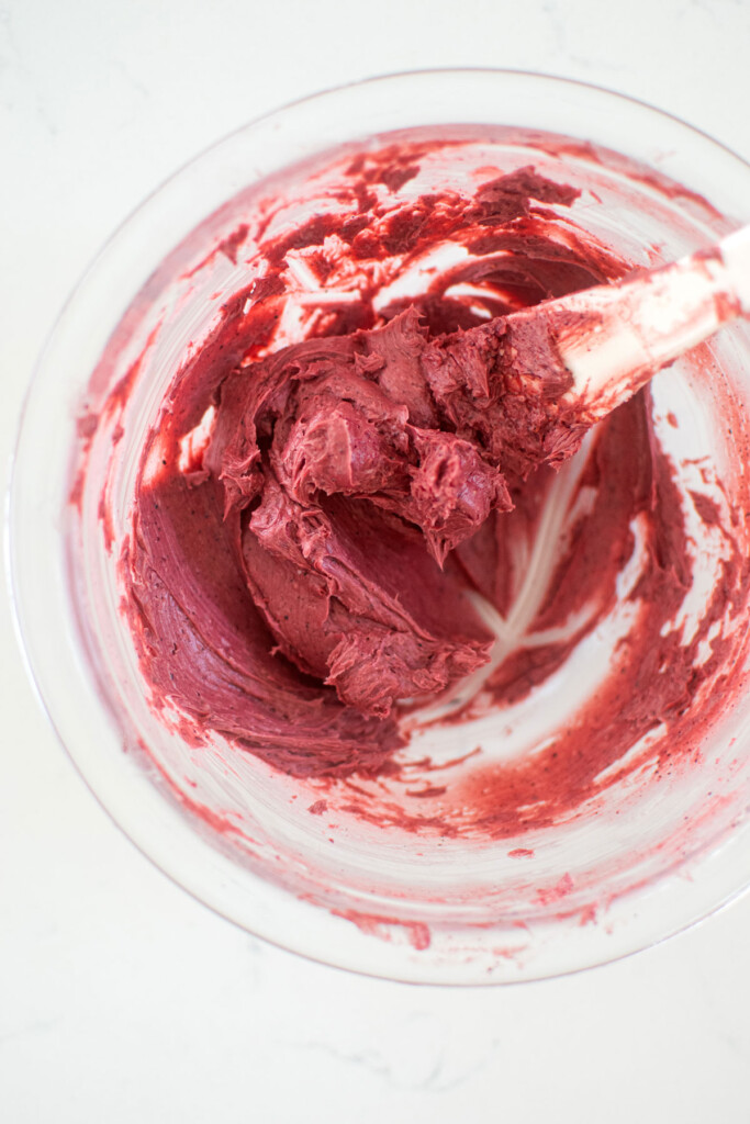 blueberry butter spread being mixed together in a glass mixing bowl on a white marble counter.