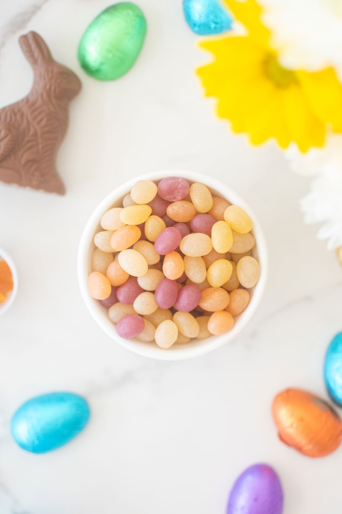 organic jelly beans in a small bowl on a white marble counter with a chocolate easter bunny and eggs.