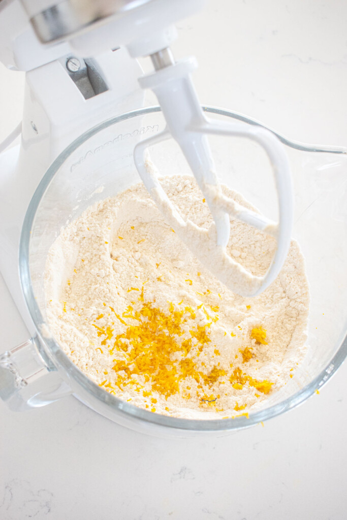 ingredients for lemon cake in a glass mixing bowl on a white marble counter.