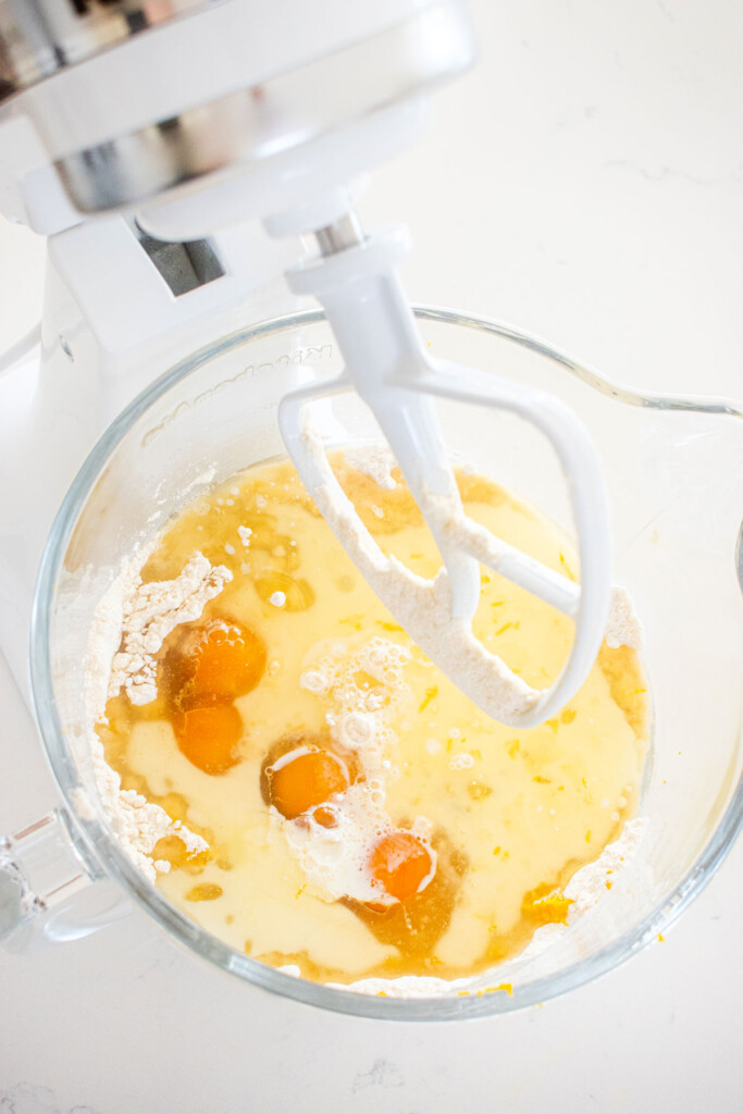 ingredients for lemon cake in a glass mixing bowl on a white marble counter.