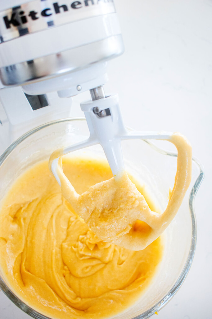 lemon cake batter in a glass mixing bowl on a white marble counter.