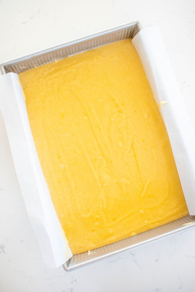 lemon cake batter in a cake pan on a white marble counter.