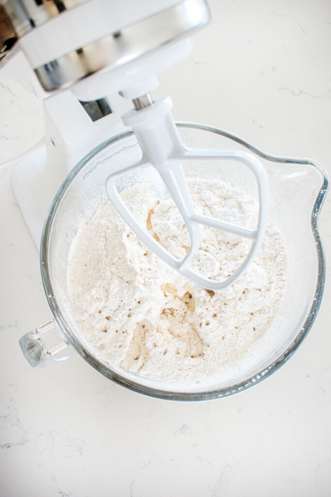 buttercream frosting ingredients in a glass mixing bowl on a white marble counter.