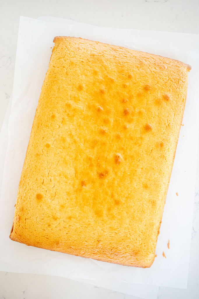baked lemon sheet cake on a piece of parchment paper on a white marble counter.