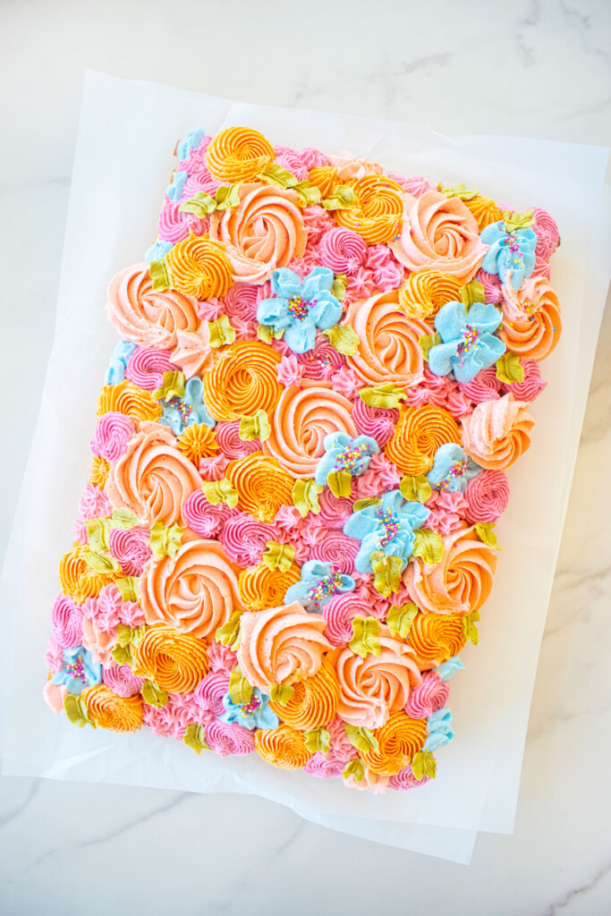 flower sheet cake with different colored buttercream flowers on a white marble counter.