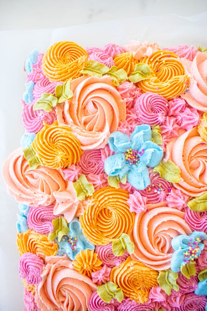 flower sheet cake with different colored buttercream flowers on a white marble counter.