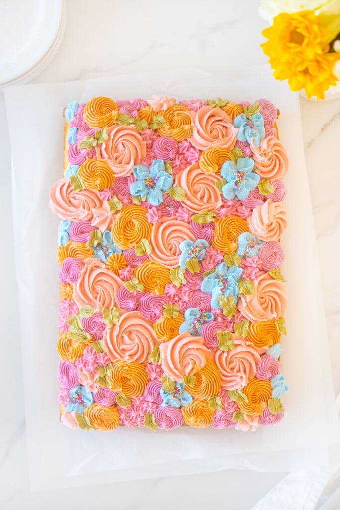 flower sheet cake with different colored buttercream flowers on a white marble counter.