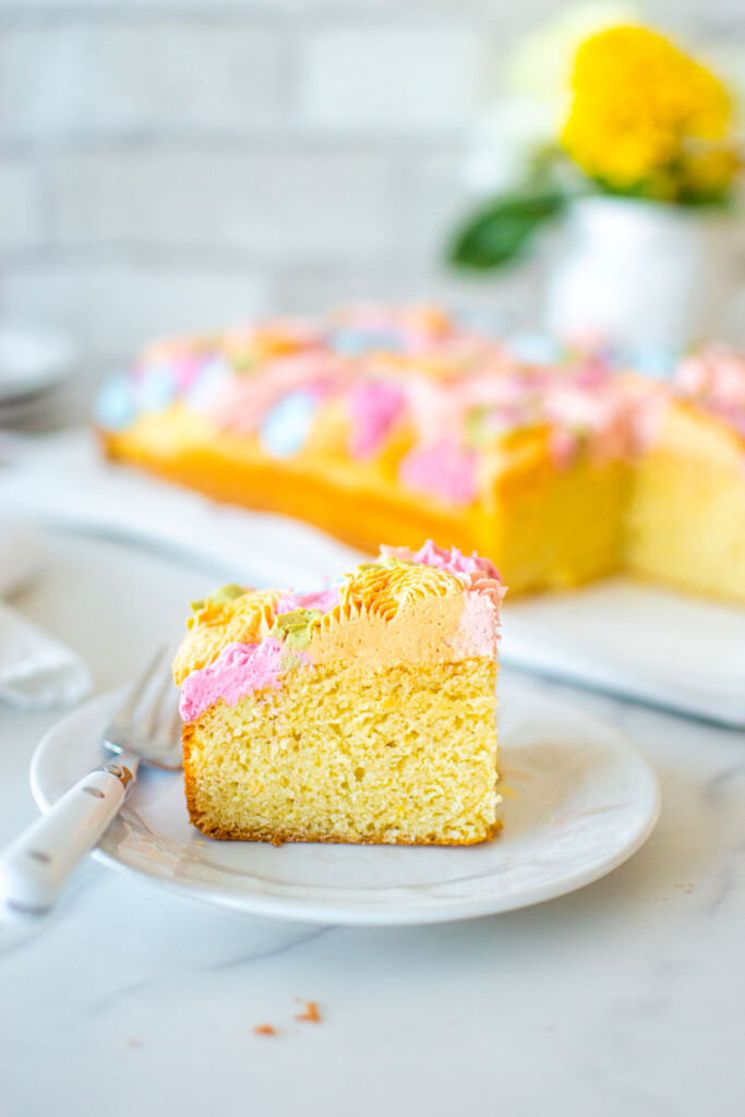 slice of pastel colored flower sheet cake on a plate on a white marble counter.