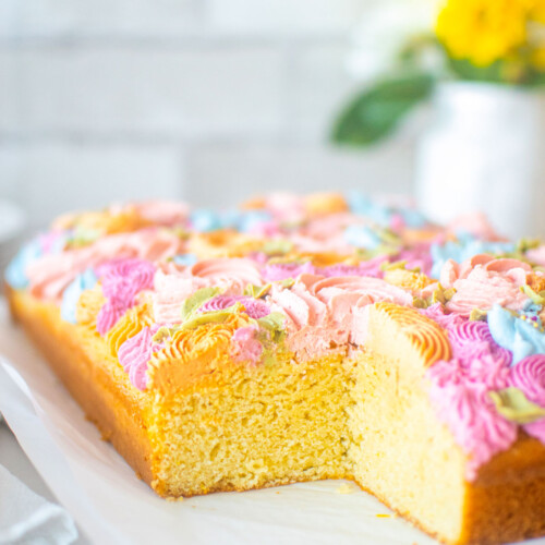 pastel flower sheet cake cut on a white marble counter with fresh flowers.