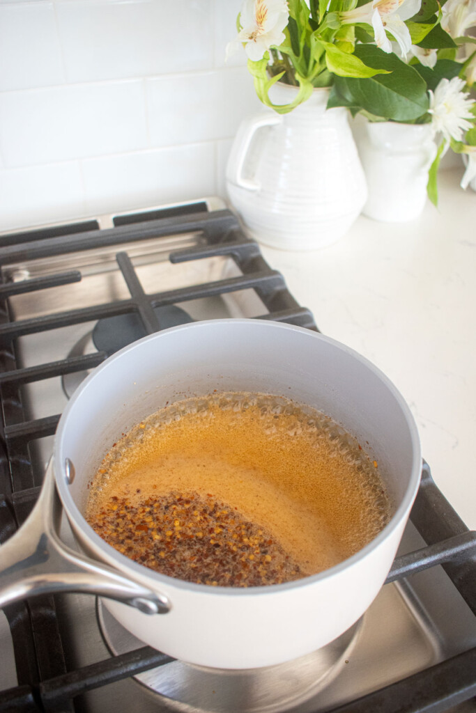 homemade organic hot honey being cooked in a small pot over the stovetop.