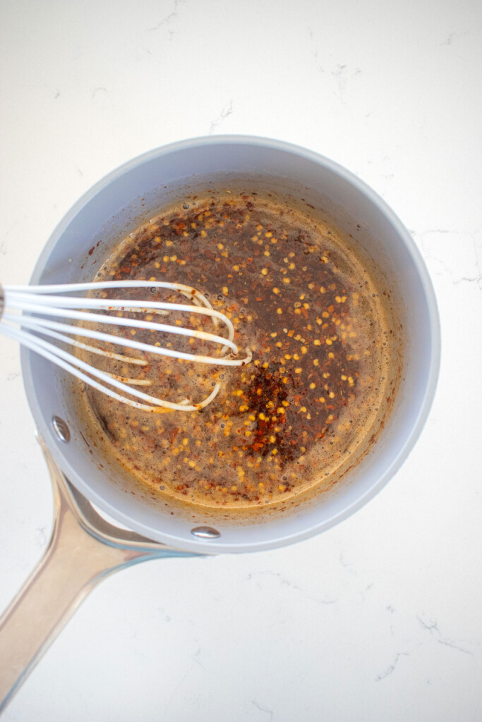 homemade organic hot honey in a small pot on a white marble counter with a whiek.