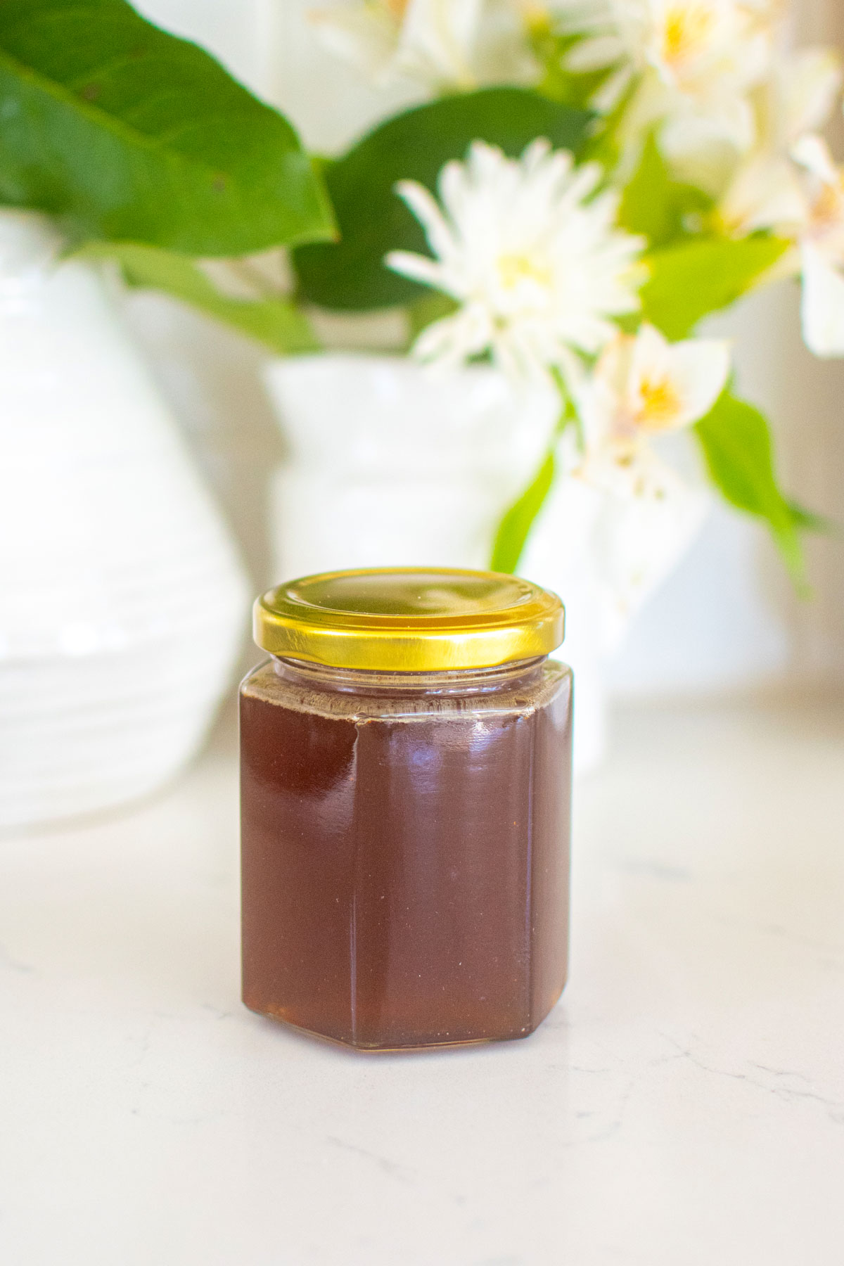 homemade organic hot honey in a glass honey jar on a marble counter with fresh flowers.