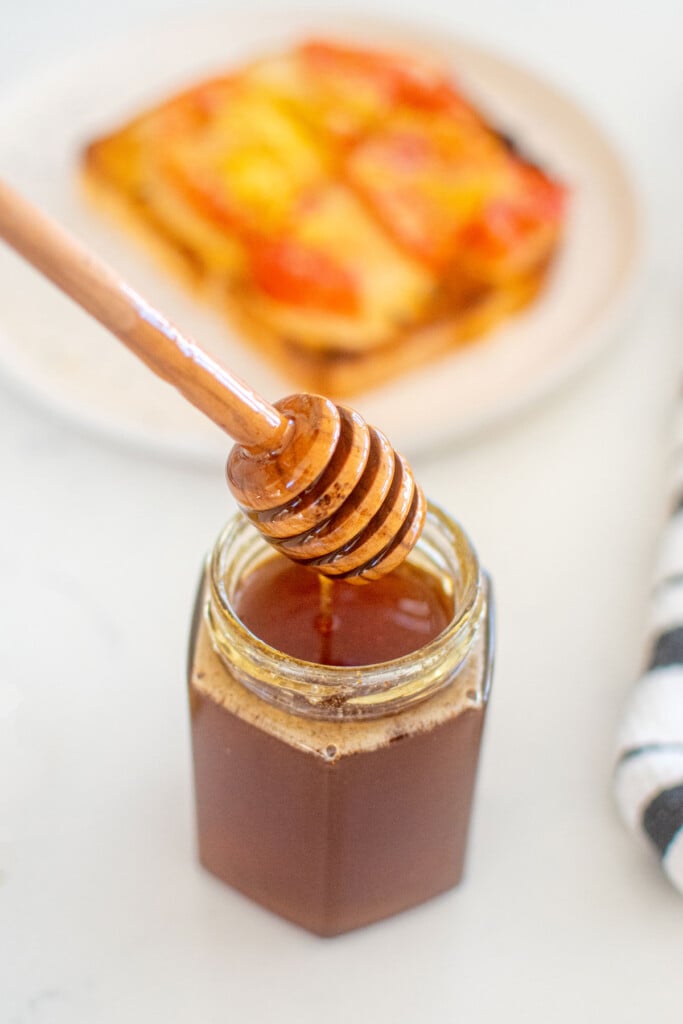 homemade organic hot honey jar with a honey dipstick on a white marble counter.