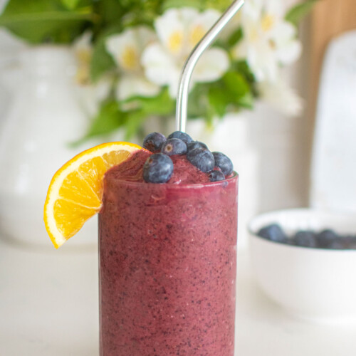 lemon blueberry smoothie with fresh lemon slice and blueberries in a glass on a white kitchen countertop.