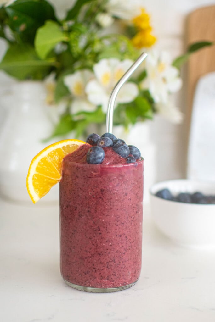 lemon blueberry smoothie with fresh lemon slice and blueberries in a glass on a white kitchen countertop.
