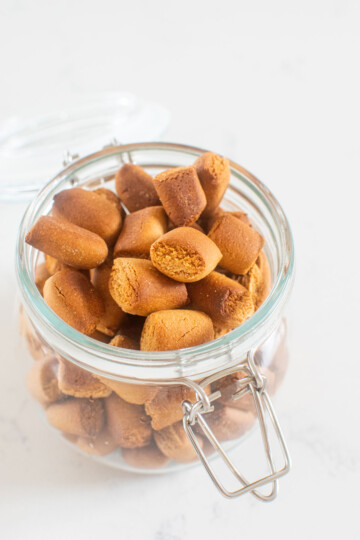 mini peanut butter oat dog treats in a glass container on the kitchen counter.