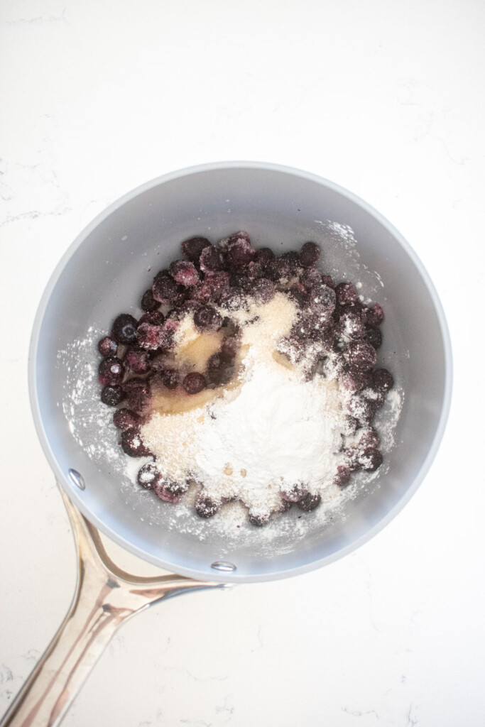 blueberry jam filling in a small pot on a white marble counter.
