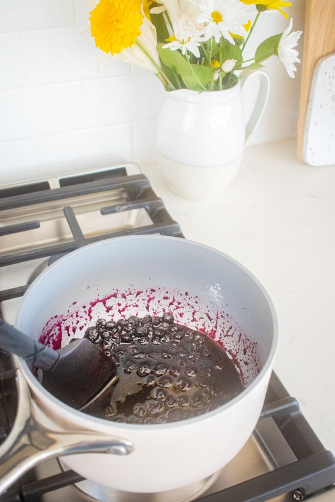 blueberry jam being cooked in a small pot over the stovetop.