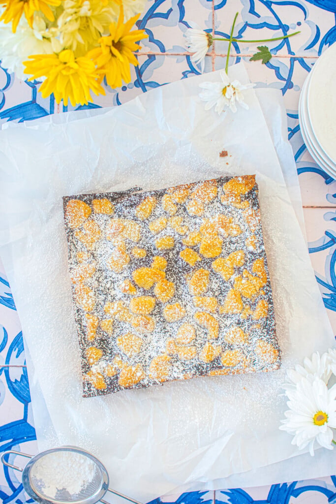 sourdough blueberry crumb bars on white parchment paper on a blue tile table.